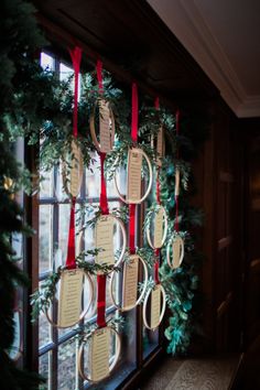 a christmas wreath hanging on the side of a window with red ribbon and tags attached to it