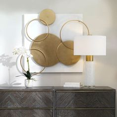 a white vase sitting on top of a wooden dresser next to a painting and lamp