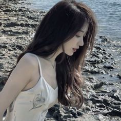 a young woman standing on top of a beach next to the ocean holding a cell phone