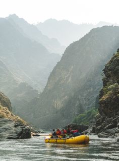 a group of people riding on the back of a yellow raft down a river surrounded by mountains