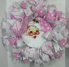 a pink and white christmas wreath with santa claus on it's face, surrounded by silver ribbons