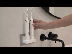 two electric toothbrushes are attached to the wall and being held by someone's hand