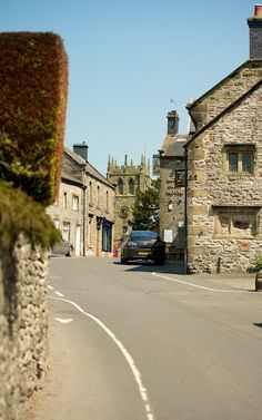 a car parked on the side of a road in front of some stone buildings and trees