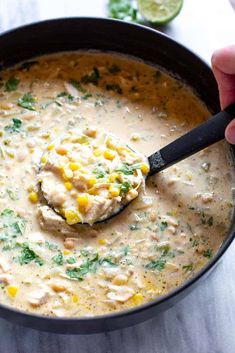 a hand holding a ladle full of chicken and corn chowder in a skillet