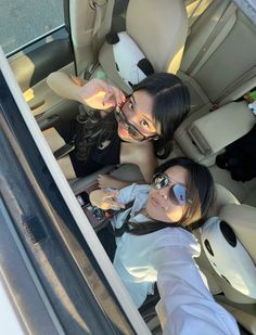 two women sitting in the back seat of a car taking a selfie with their cell phone