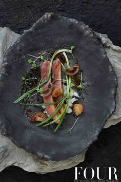 a black plate topped with meat and veggies on top of a stone slab