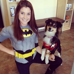 a woman is posing with her dog dressed up as batgirl and the dog is wearing a costume