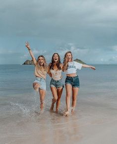 three young women are running in the water at the beach and one is holding her arms up