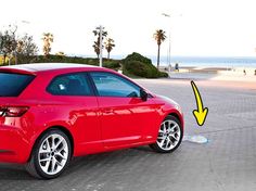 the red car is parked on the side of the road next to the ocean and palm trees