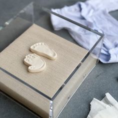 a clear box with two baby footprints on it and some cloths next to it