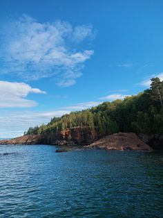 an island in the middle of water with trees on both sides and blue sky above