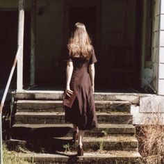 a woman in a dress walking up the steps to an old house with her purse