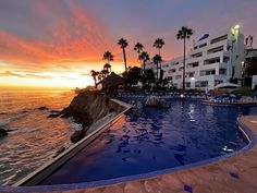 an outdoor swimming pool next to the ocean with palm trees and buildings in the background