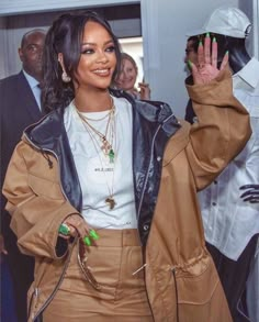 a woman with green nails waves at the camera while wearing a brown jacket and skirt