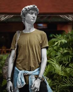 a statue of a young man with his hands in his pockets, standing next to some plants