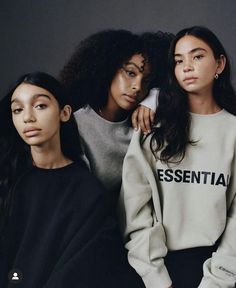 three young women sitting next to each other in front of a gray wall wearing sweatshirts