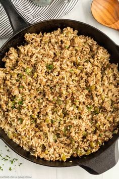 a skillet filled with rice and vegetables on top of a counter next to a wooden spoon