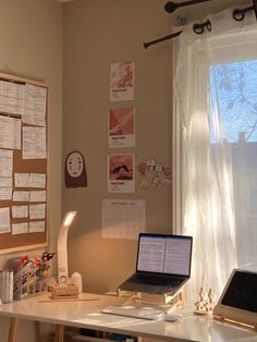 a laptop computer sitting on top of a white desk next to a lamp and window