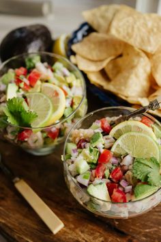 two bowls filled with salad and chips on top of a wooden cutting board next to a bowl of tortilla chips