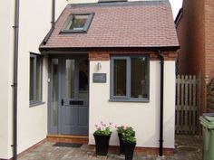 a small white house with two plants in the front and one planter on the side