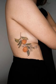 a woman's stomach with an orange and leaves tattoo on the side of her body