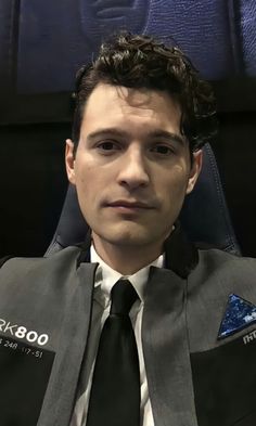 a man wearing a suit and tie sitting in front of a blue wall with the words nasa on it