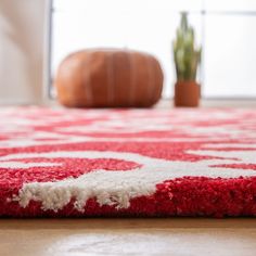 a red and white rug sitting on top of a wooden floor next to a potted plant