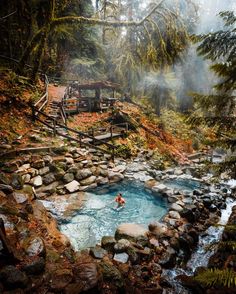 a hot spring in the middle of a forest filled with rocks and water, surrounded by trees