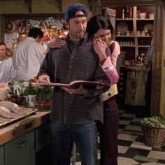 a man and woman standing in a kitchen next to each other looking at a menu