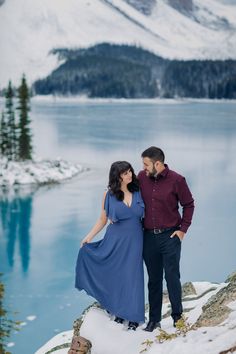 a man and woman standing next to each other on top of snow covered ground near water