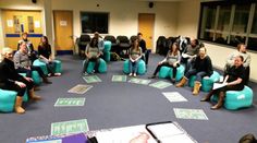 a group of people sitting on bean bags in a room with blue carpet and chairs