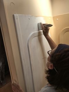 a woman is painting the side of a white refrigerator with a paint roller and brush