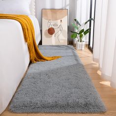 a white bed with a gray rug on top of it and a yellow blanket next to it