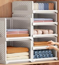 a person reaching for folded towels in a closet with shelving and shelves on the wall