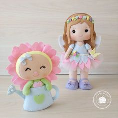 two little dolls sitting next to each other on top of a wooden table and one has a flower in her hand