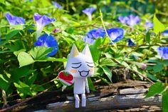 a small white cat figurine sitting on top of a log in front of blue flowers