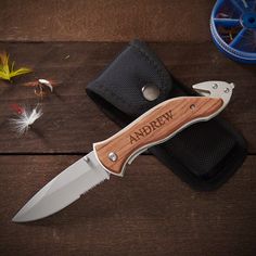 a knife with a wooden handle sitting on top of a table next to some fishing flies