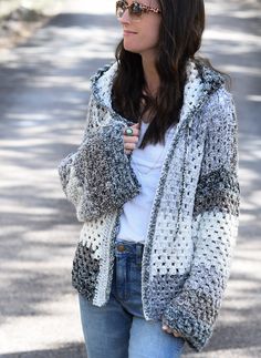 a woman standing in the street wearing jeans and a jacket with an open hoodie