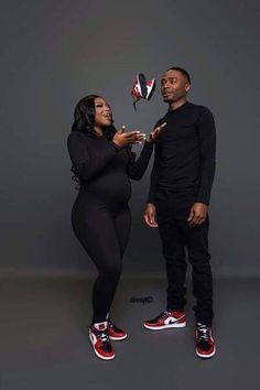 a man and woman standing next to each other in front of a gray background with red shoes