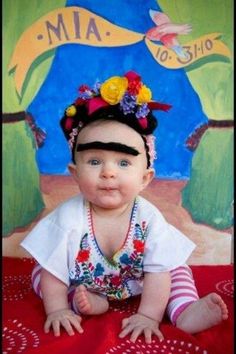 a baby is laying on a red blanket wearing a headband and flowers in her hair