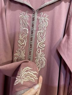 a woman's hand is holding onto a pink shirt with white embroidery on it