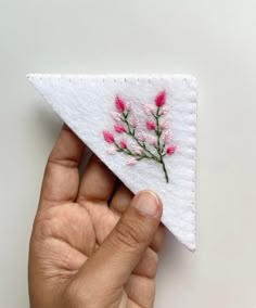 a hand is holding a piece of cloth with pink flowers on it and white background