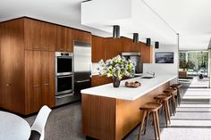 a modern kitchen with wooden cabinets and white counter tops, along with bar stools