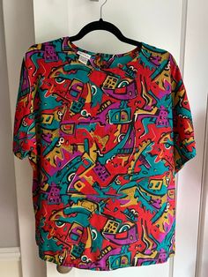 "DESCRIPTION:  Stylish and modern (for the early 90s) busy-patterned blouse. 100% polyester, but feels like silk. Double button closure in the back of the neck. Very slightly see-though. CONDITION: very good condition, no flaws that I can see MEASUREMENTS:  bust 36\", sleeve 8\", shoulders 14.5\", length 25\", waist 42\" Thanks for visiting Secondhand UFOs!  **Everything I sell is pre-owned vintage or antique and may show signs of previous use. Any props are for display purposes only and are not Retro Patterned Tops With Vibrant Print, Short Sleeve Multicolor Abstract Print Blouse, Multicolor Abstract Print Short Sleeve Blouse, Retro Multicolor Graphic Print Blouse, Patterned Abstract Print Short Sleeve Blouse, Patterned Short Sleeve Blouse With Abstract Print, Retro Abstract Print Patterned Blouse, Retro Abstract Print Patterned Tops, Vintage Multicolor Blouse With Abstract Print