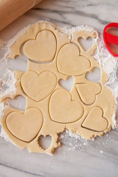 heart shaped cookie cutters sitting on top of flour next to a rolling pin and red scissors