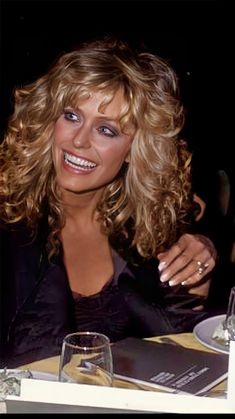 a woman sitting at a table with a glass in front of her and smiling for the camera