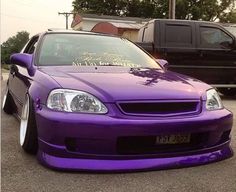 a purple car parked in a parking lot next to two other cars with writing on the hood