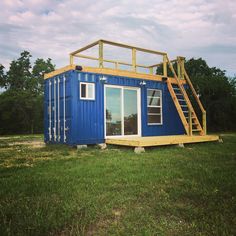 a blue shipping container sitting in the middle of a field with stairs leading up to it