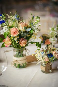 two vases filled with flowers sitting on top of a white tablecloth covered table