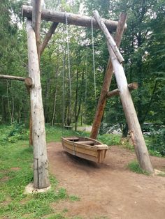 a wooden swing set in the middle of a wooded area with swings and benches on it